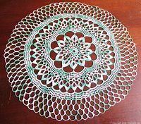 Full view of round green and white crochet doily on table surface