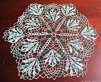 Full overhead view of entire green and white crochet doily on wood surface