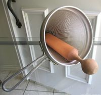 Aluminum cone strainer resting on glass table with wood pestle inside