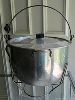 Front view of Supreme aluminum stock pot on wire stand showing bail handle and lid