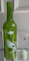 Full view of green glass bottle with bird design and included candle beside it