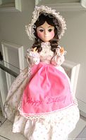 Full view of Bradley paper mache doll in floral hoop skirt dress and pink Happy Birthday apron
