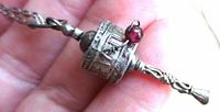 Close view of pendant showing embossed mantra, red bead, handle