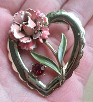 Front view showing heart outline, enamel flower, leaves and red rhinestone