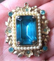Front view showing aquamarine glass stone, faux pearls, floral frame, blue rhinestones