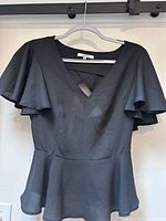 Front view of black BB Dakota blouse on hanger showing cutout, flutter sleeves, peplum hem