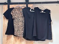 Four tops on hangers: two black T-shirts, leopard print blouse, black sleeveless blouse