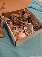 Open cardboard box showing loose sports trading cards padded with brown packing paper