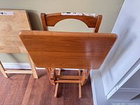 Two folded wooden TV trays leaning against wall
