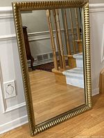 Full front view of gilt ripple frame mirror leaning against wall