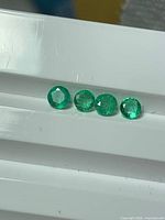 Four round vivid green emeralds aligned on white surface