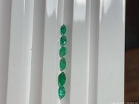 Six marquise emeralds aligned vertically on white background