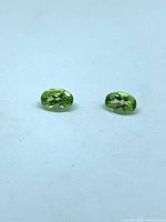 Front view of two oval green peridot stones on white background