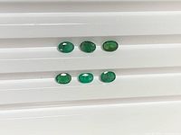 Six oval green emeralds on white background