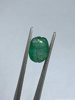 Emerald face-up held by tweezers showing color and inclusions