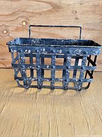 Full view of rectangular metal basket showing grid design, handle, chipped paint, and rust