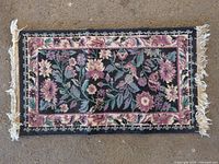 Full view of small black floral rug showing size and fringe