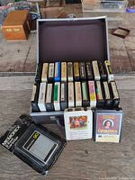 Open metal case showing two rows of assorted 8-track cartridges plus additional cartridges and sealed Memorex blank in front