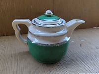 Front view of green and cream porcelain teapot with silver trim