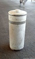 Full view of cylindrical white enamel umbrella stand with lid showing rust spots and pierced band