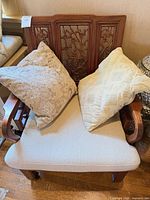 Front view of carved wooden armchair with two beige pillows