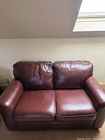 Front view of the brown leather loveseat showing overall design and cushions