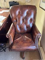 Front view of brown leather tufted executive office chair with nailhead trim and wood base on casters