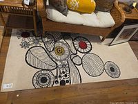 Full view of ivory rug under wicker sofa showing black abstract pattern with red/yellow accents