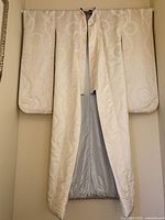 Front view of full-length ivory silk Japanese wedding kimono hung open showing lining and pattern