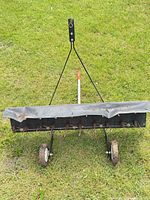Front view of Brinly tow-behind rake showing full width, hitch arm and wheels