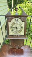 Front view of complete Bulova wooden wall clock on balcony railing