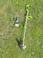 Full view of string trimmer with battery and charger on grass