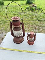 large and small red metal hurricane lanterns on table with tape measure