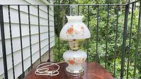 Full view of floral milk glass hurricane table lamp on table
