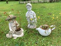 Group view of both garden statues and ceramic teapot planter on lawn