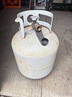 Front view of white steel propane cylinder showing surface rust and overall condition