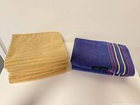 Stack of five gold/mustard towels beside folded purple-blue towel