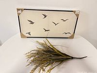 Framed bird print in packaging alongside artificial grass spray
