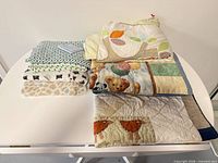Stack of six crib quilts and blankets showing variety of patterns and colours