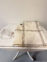 Folded ivory plaid heated throw on table with cord attached