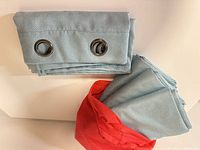 Folded curtain panels showing metal grommets beside red bag