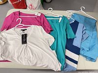 Five clothing pieces on table: white tee, magenta tee, teal top, striped pullover, blue pants