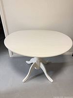 Full view of white round pedestal dining table with leaves up