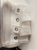Folded stack of four white polyester curtain panels showing grommet headers