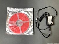 Sealed spool of pink LED rope light beside included AC adapter