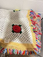 Entire afghan folded showing white granny squares, red flower, yellow border, multicolour fringe
