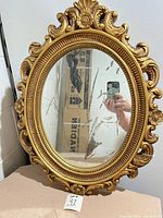 Front view of ornate gold oval mirror showing frame design and glass condition