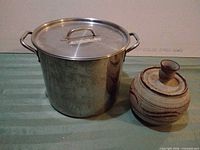 Stainless steel stock pot beside pottery crock with lid on