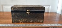Front view of rectangular wooden box with floral pattern and metal clasp, ruler for scale