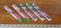Five blister-packed purple GUM toothbrushes lined beside ruler